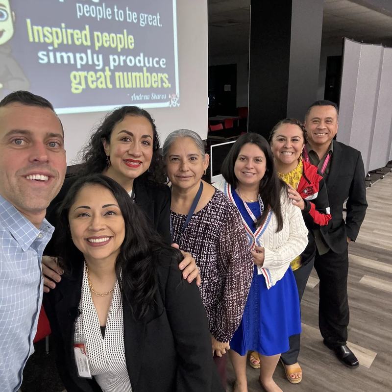 Andrew Sharos taking a selfie with a group of educators in front of a presentation slide
